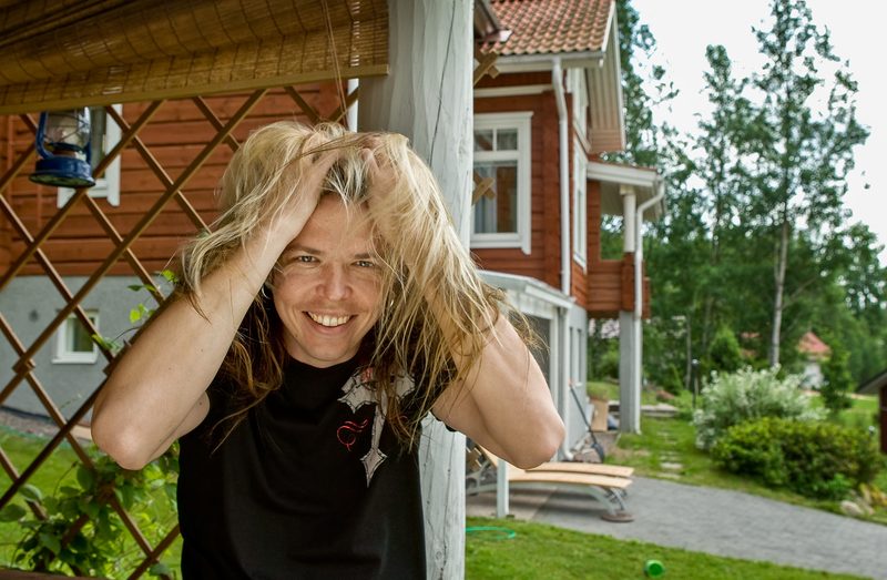 Eicca Toppinen pitelee hiuksiaan punaisen talon pihalla