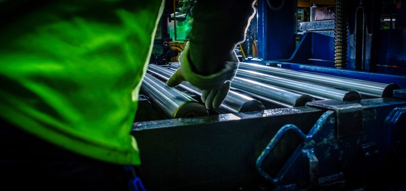 Vihreähihainen työntekijä tarkastaa teräsputkia rullaradalla